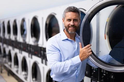 Man handling housework and workload. Man doing laundry and working on laptop Stock Photos