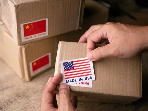 Man Hands applying MADE IN USA over MADE IN CHINA label on a shipping cardb.. 스톡 사진