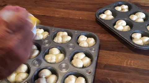 Man hands brushing clover leaf rolls with butter in preparation for baking. Stock Footage 130387614