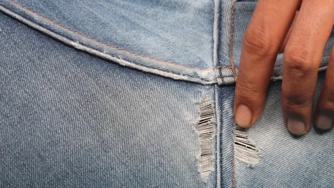 Man hands checking torn denim jeans at back seam while sitting Stock Footage 348579376