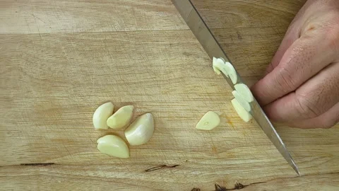 Man hands chopping raw garlic on a scratched wooden cutting board with a ki.. 스톡 동영상 318010356