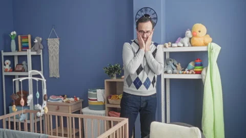 Man with hands clasped near face by wooden crib and hanging mobile in build.. Video stock 337443290