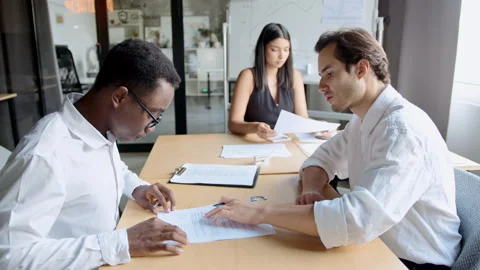 Man hands a contract to a black man, explaining where to sign for the purchase 스톡 동영상 335733407