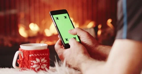 Man Hands with Cup Using SmartPhone by the Burning Fireplace. 4K SLOW MOTION Vidéo 69259963