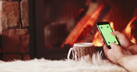 Man Hands with Cup Using SmartPhone by the Burning Fireplace. 4K SLOW MOTION Vidéo 69261562