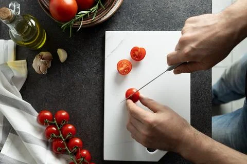 Man hands cutting cherry tomatoes on kitchen countertop Stock Photos