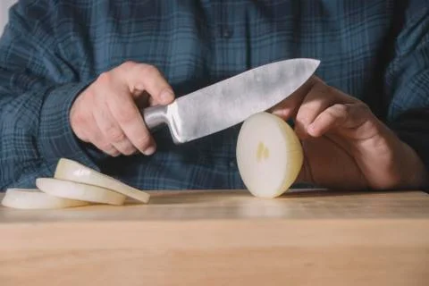 Man hands cutting with a sharp knife an onion in slices on a wooden table. Bu Stock Photos