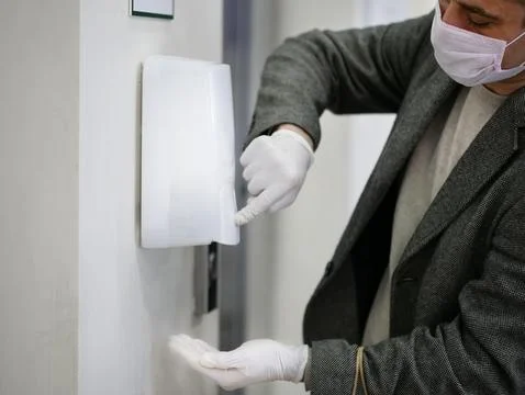 Man hands in gloves Using Automatic Alcohol Dispenser to Clean Bacteria and Stock Photos