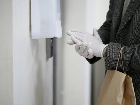 Man hands in gloves Using Automatic Alcohol Dispenser to Clean Bacteria and Stock Photos