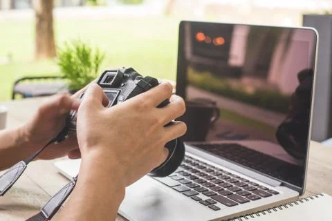Man hands hand holding camera and using laptop computer in coffee shop. Stock Photos