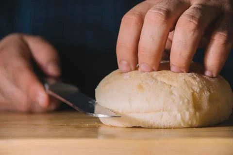 Man hands holding a bread bun and cutting it with a serrated stainless steel  Stock Photos