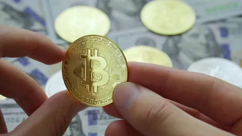 Man hands holding crypto currency golden Bitcoin coin above dollars background Stock Footage 200770406