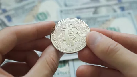 Man hands holding crypto currency silver Bitcoin coin above dollars background Stock Footage 204129010
