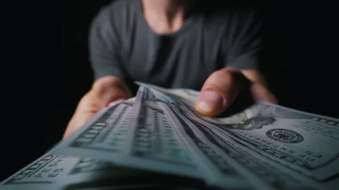 Man Hands Holding Out Fan of One Hundred Dollar Bills in Dark Room Stock Footage 339366495