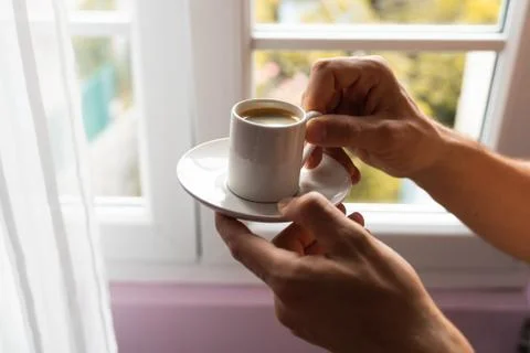 Man hands holding small cup of coffee near window in autumn morning Stock Photos