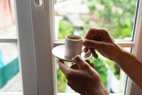 Man hands holding small cup of coffee near window in morning sunlight Stock Photos