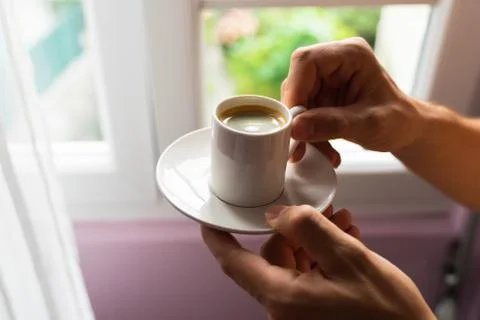 Man hands holding small cup of coffee near window in morning sunlight Stock Photos
