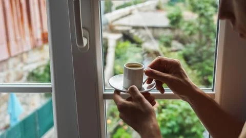 Man hands holding small cup of coffee near window in morning sunlight Stock Photos