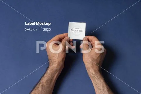 A man hands holding a small label in front of dark blue background mock-up se PSD Template