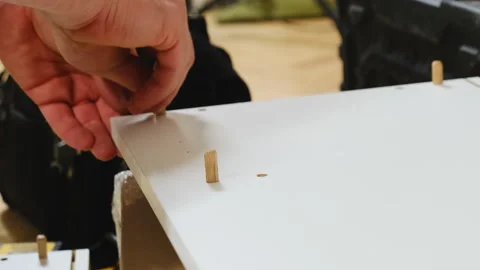 Man hands insert wooden pins into hole of white plywood wall Video stock 304397014