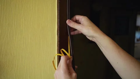 Man hands installing insulation tape on a wooden door frame slow motion Stockbeeldmateriaal 347437360