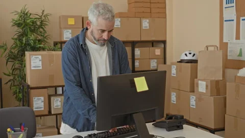 Man with hands on keyboard at computer desk surrounded by stacked cardboard.. Stock Footage 347861076