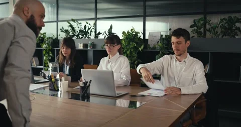 Man hands out documents to colleagues during a team meeting in a modern office Stock Footage 317402694
