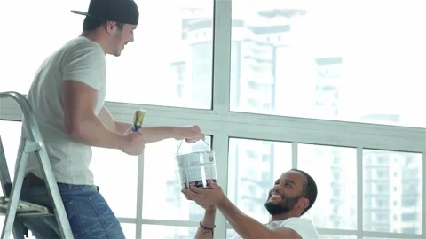 A man hands paint to another man on a ladder during apartment renovations Stock Footage 311816613
