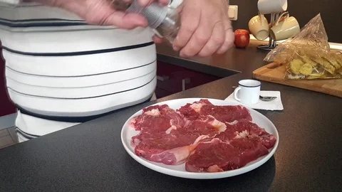 Man hands pepper red meat abundantly on white ceramic plate Stock Footage 108605105