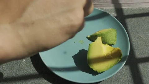 Man hands put avocado in a blue plate on a sunny day the shadow of the grid Stock Footage 232185824