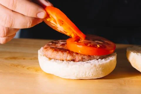 Man hands putting on a burger two slices of tomato on a wooden board. Cooking Stock Photos