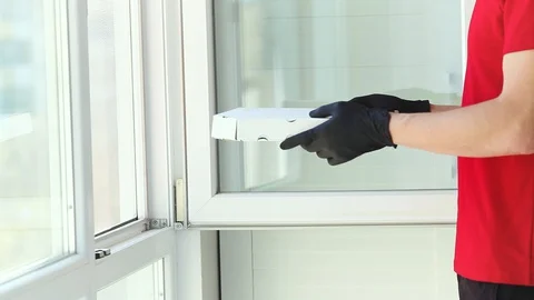 A man hands rubber gloves with a box pizza near the window . Stock Footage 128986148