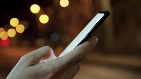 Man hands texting on a smartphone in the night city on background.Connecting and Stock Photos