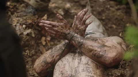 Man With Hands Tied In Cable Tie And A Sack Over His Head Lies In A Dirt Pit Video stock 328946681