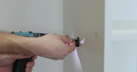 Man hands use electric screwdriver for installing screws into holes of shelf Видео 329763371
