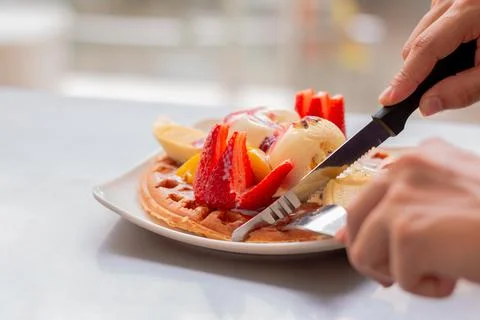 Man hands using cutlery to cut delicious fruit pancake with ice cream. Colombian Stock Photos