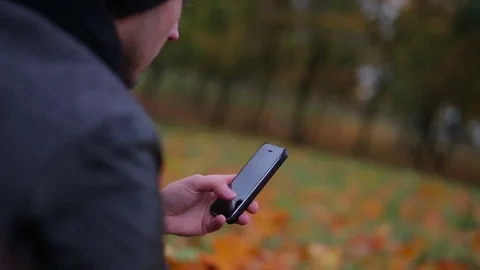 Man hands using smartphone touchpad typing sms message in autumn park sitting on Stock Footage 73905660