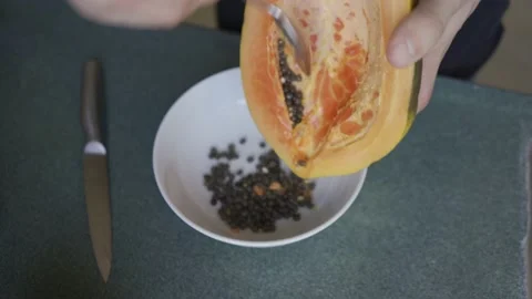 Man hands using a spoon to remove the seeds from a papaya. HLG3, BT.2020 Stock Footage 231172735