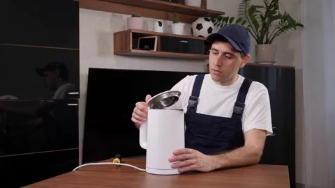A man handyman repairs a broken electric kettle while sitting at a table. Stock Footage 287588208