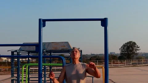 Man Hanging and Stretching from a Pull Up Bar at an outdoor Fitness Park Stock Footage 284164197