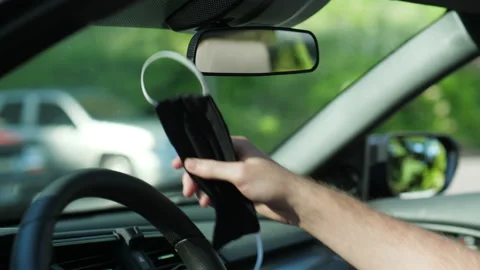 Man hanging black face mask on car rear view mirror Stock Footage 133341164