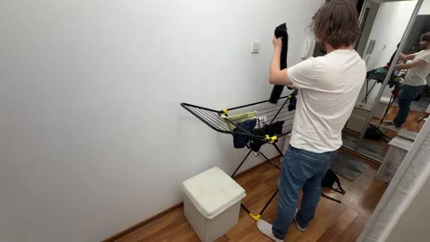 Man hanging freshly washed clothes on a drying rack in a narrow hallway at home, Stock Footage 336981442