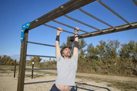 Man hanging on metal bars while exercising grip strength outside Stock Photos