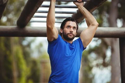 Man hanging from rust-colored horizontal bars in park fitness area under soft Fotos Stock