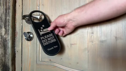 Man hanging sign with text "Please do not disturb" from handle of door Stock Footage 308343096
