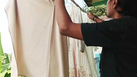 Man Hanging Wet Laundry to Dry Outdoors on a Sunny Day Stock Footage 334166828