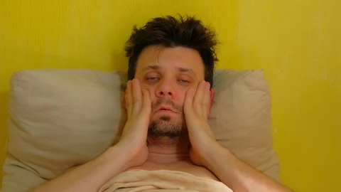 Man with hangover claps on cheeks to wake up lying in bed, portrait closeup. Stock Footage 128705504