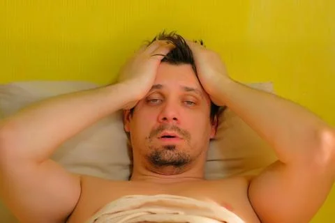 Man with hangover claps on cheeks to wake up lying in bed, portrait closeup. Stock Photos