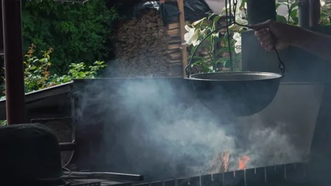 Man hangs a cauldron over the grill for cooking on a campfire. Stock Footage 167858569