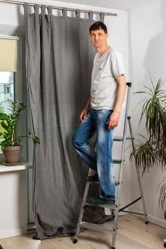 A man hangs curtains Stock Photos
